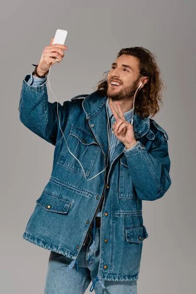 Smiling man in denim jacket taking selfie and showing peace sign isolated on grey — Stock Photo