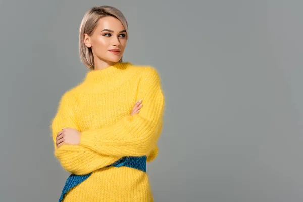 Atractiva mujer en vestido amarillo con los brazos cruzados mirando hacia otro lado aislado en gris - foto de stock