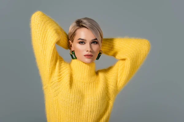 Atractiva mujer en vestido amarillo con pendiente mirando a la cámara aislada en gris - foto de stock