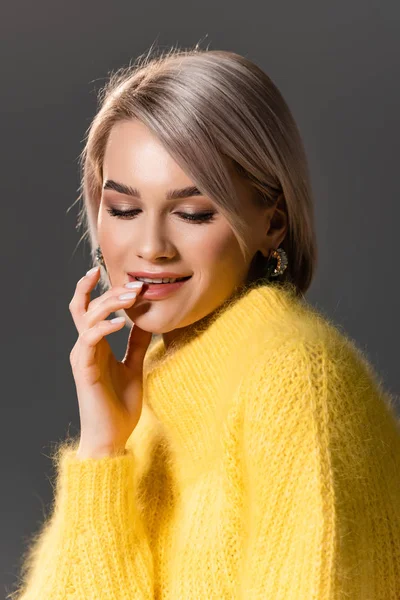 Attraktive und lächelnde Frau in gelbem Kleid, die Lippen isoliert auf grau berührt — Stockfoto
