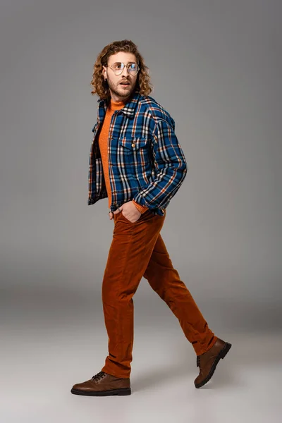 Homme choqué en chemise avec la main dans la poche marchant sur fond gris — Photo de stock