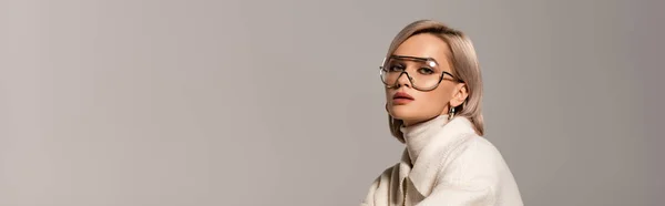 Prise de vue panoramique d'une jolie femme en manteau et lunettes regardant la caméra isolée sur gris — Photo de stock