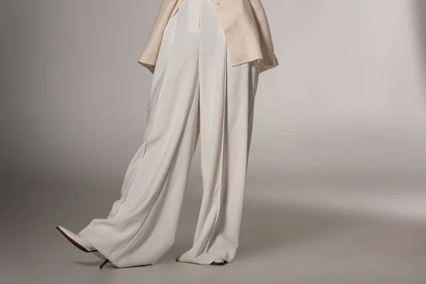 Обрезанный вид стильной женщины в белых брюках на сером фоне — стоковое фото