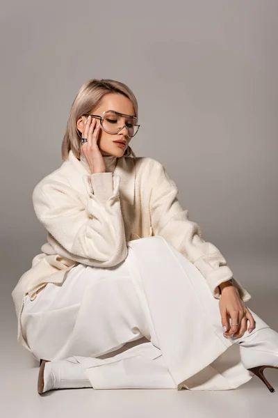 Attractive woman in white coat and trousers sitting on grey background — Stock Photo