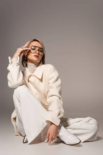 Jolie femme en manteau blanc et pantalon regardant la caméra sur fond gris — Photo de stock