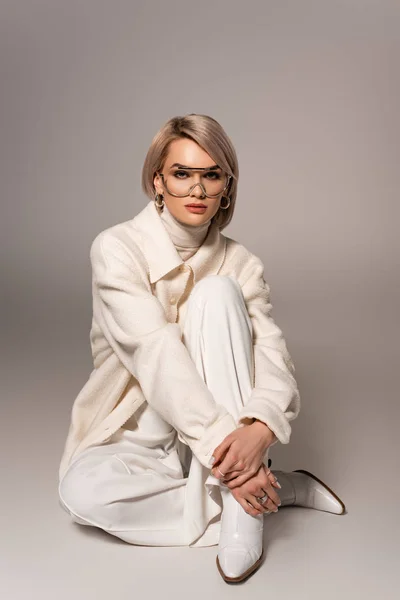 Jolie femme en manteau blanc et pantalon regardant la caméra sur fond gris — Photo de stock