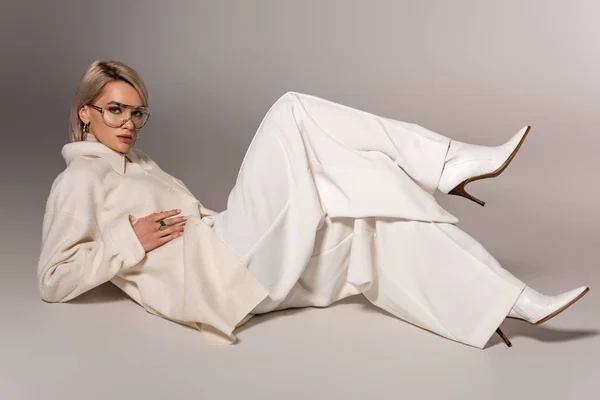 Jolie femme en manteau blanc et pantalon regardant la caméra sur fond gris — Photo de stock