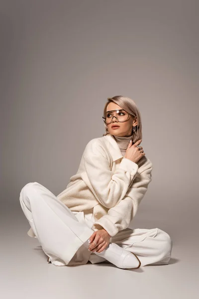 Mulher atraente em casaco branco e calças olhando para longe no fundo cinza — Fotografia de Stock