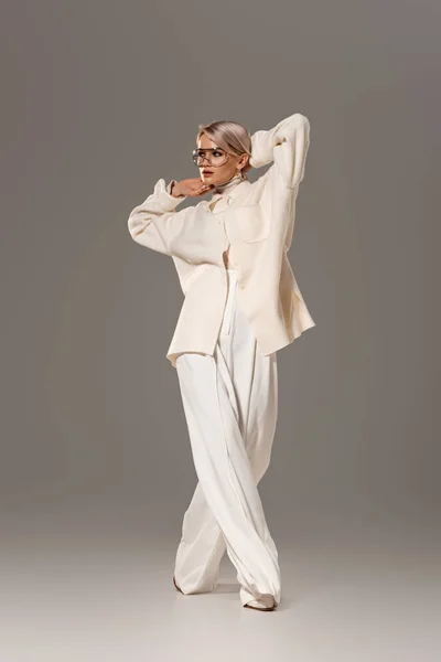 Привлекательная женщина в белом халате и брюках, смотрящая в сторону на сером фоне — стоковое фото