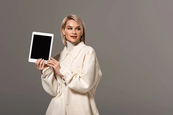 Attraktive und lächelnde Frau in weißem Mantel mit digitalem Tablet isoliert auf grau — Stockfoto