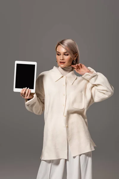 Attractive and smiling woman in white coat holding digital tablet isolated on grey — Stock Photo