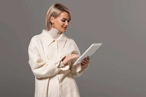 Attractive and smiling woman in white coat using digital tablet isolated on grey — Stock Photo