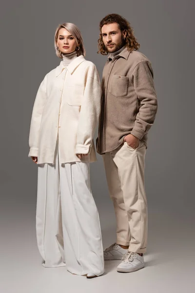 Woman in white coat and man in shirt with hand in pocket looking at camera on grey background — Stock Photo