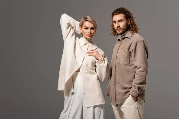 Frau in weißem Mantel und Mann im Hemd mit der Hand in der Tasche schauen vereinzelt in die Kamera auf grau — Stockfoto