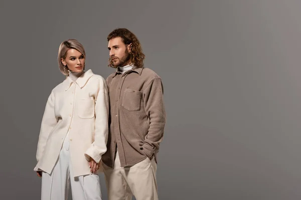 Женщина в белом пальто и мужчина в рубашке с рукой в кармане изолированы на сером — стоковое фото