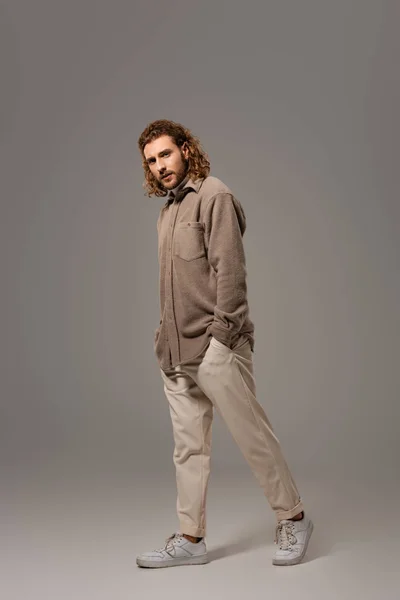 Hombre guapo en camisa y pantalones caminando sobre fondo gris - foto de stock