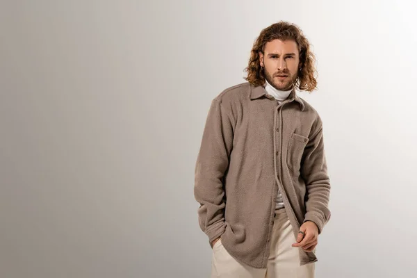 Hombre guapo en camisa con la mano en el bolsillo mirando a la cámara sobre fondo gris - foto de stock