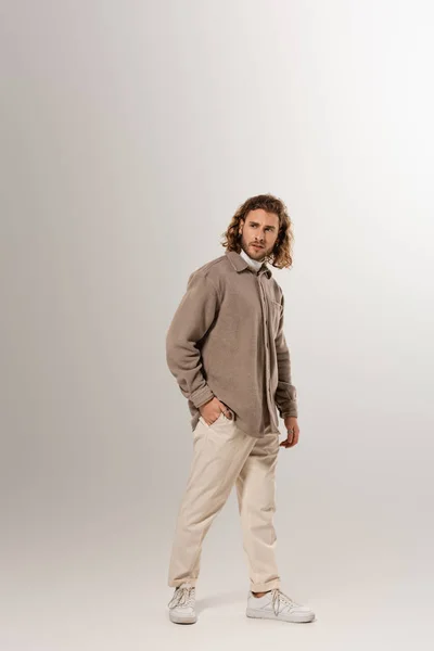 Homem bonito na camisa e calças olhando para longe no fundo cinza — Fotografia de Stock