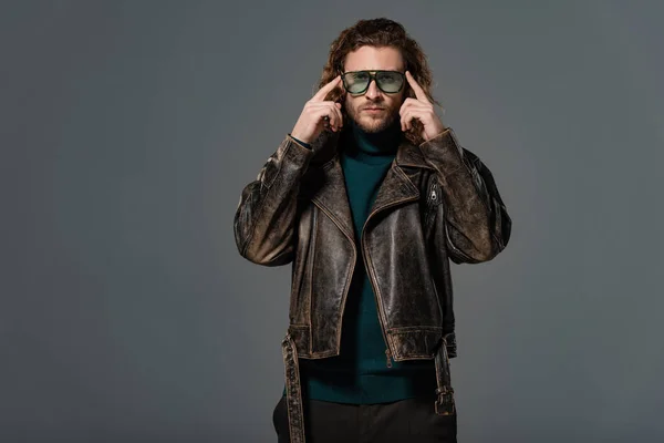 Handsome man in leather jacket touching sunglasses isolated on grey — Stock Photo