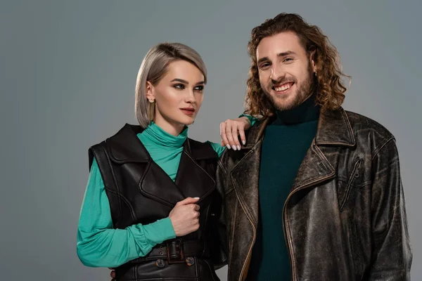 Woman in vest touching smiling man in leather jacket isolated on grey — Stock Photo