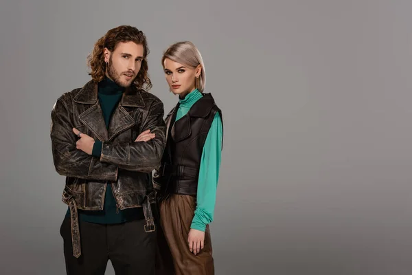 Woman in vest and man in leather jacket with crossed arms looking at camera isolated on grey — Stock Photo