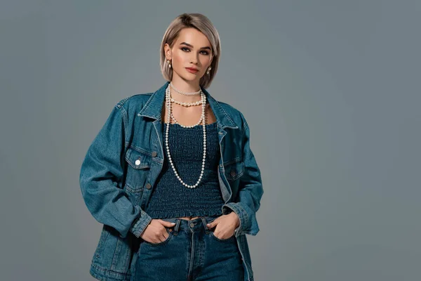 Attractive woman in denim jacket with hands in pocket looking at camera isolated on grey — Stock Photo