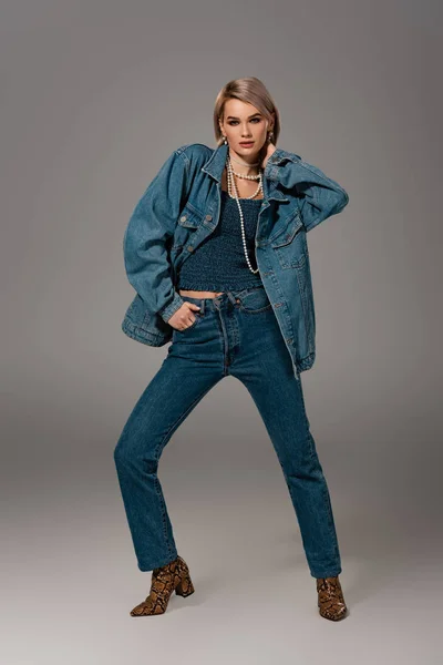 Atractiva mujer en chaqueta de mezclilla y jeans mirando a la cámara sobre fondo gris - foto de stock