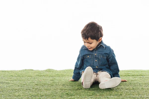 Sorrindo e bonito menino sentado na grama isolado no branco — Fotografia de Stock