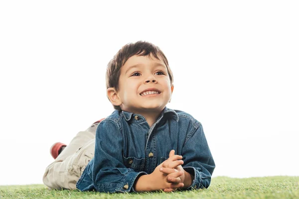 Bonito e sorridente menino olhando para longe e deitado na grama isolado no branco — Fotografia de Stock