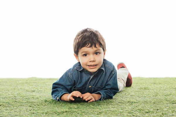 Mignon et souriant garçon regardant loin et couché sur l'herbe isolé sur blanc — Photo de stock