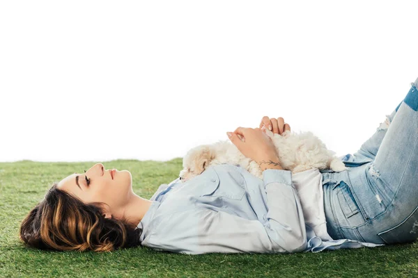 Side view of smiling woman lying on grass with Havanese puppy isolated on white — Stock Photo