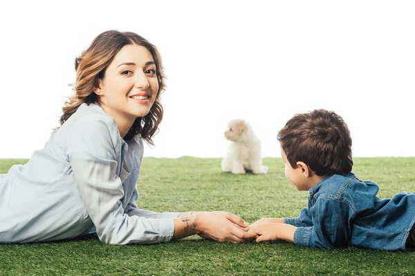 Selektiver Fokus lächelnder Mutter und Sohn auf Gras liegend und Havaneser Welpe auf weißem Hintergrund isoliert — Stockfoto