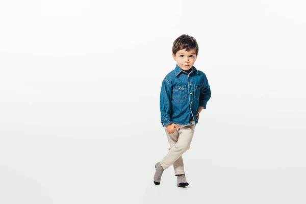 Menino bonito em camisa jeans com a mão no quadril olhando para a câmera no fundo branco — Fotografia de Stock