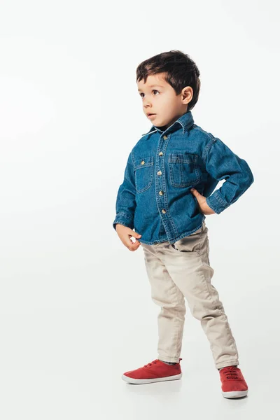 Garçon choqué en chemise en denim avec la main sur la hanche regardant loin sur fond blanc — Photo de stock