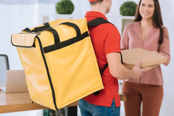Selective focus of courier with thermo backpack giving pizza boxes to smiling businesswoman — Stock Photo