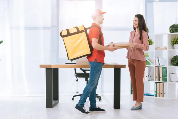 Seitenansicht des Lieferanten lächelt Geschäftsfrau an, während er Pizzakartons im Büro verteilt — Stockfoto