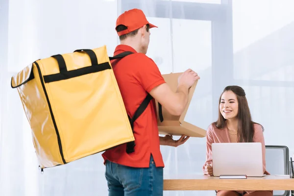 Entrega hombre mostrando pizza en caja en sonriente mujer de negocios en la mesa - foto de stock