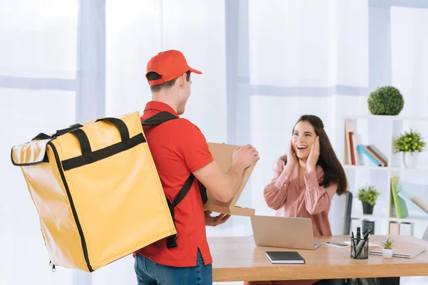 Kurier öffnet Schachtel mit Pizza bei schockierter Geschäftsfrau am Tisch im Büro — Stockfoto