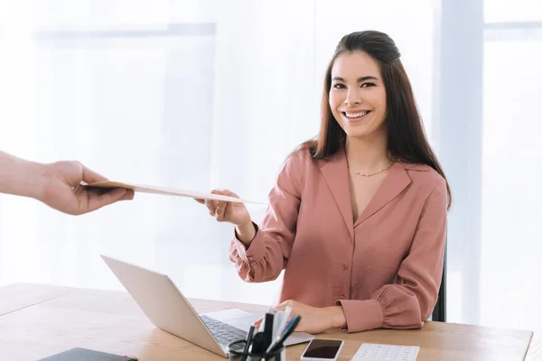 Attraktive Geschäftsfrau lächelt in Kamera neben Kurier mit Umschlag im Büro — Stockfoto