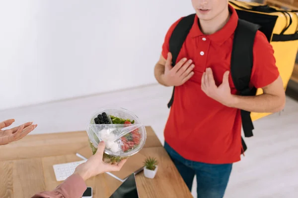 Cropped view of businesswoman with takeaway salad near confused courier — Stock Photo