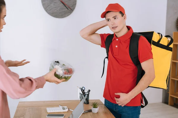 Angry businesswoman holding container with salad and looking at confused courier in office — Stock Photo