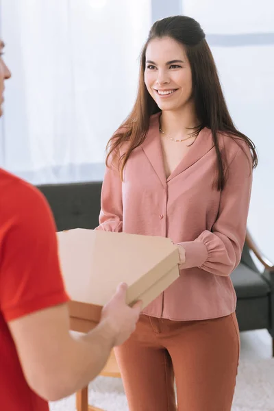Selective focus of courier giving pizza boxes to smiling woman at home — Stock Photo