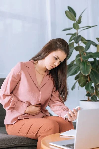 Businesswoman with hand near stomach ordering food delivery with smartphone in office — Stock Photo