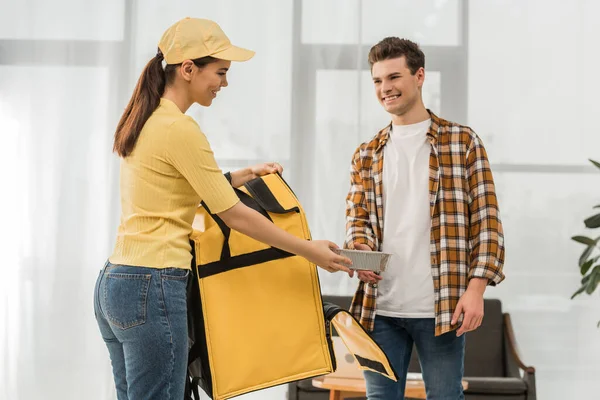 Smiling courier with thermo bag giving food container to man at home — Stock Photo