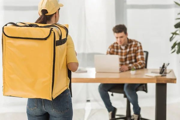Selective focus of courier with thermo backpack and businessman using laptop at table — Stock Photo