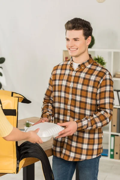 Courier with thermo bag giving food container to smiling businessman in office — Stock Photo