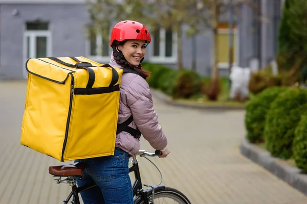 Vista lateral del atractivo mensajero con mochila térmica y bicicleta sonriendo a la cámara en la calle - foto de stock