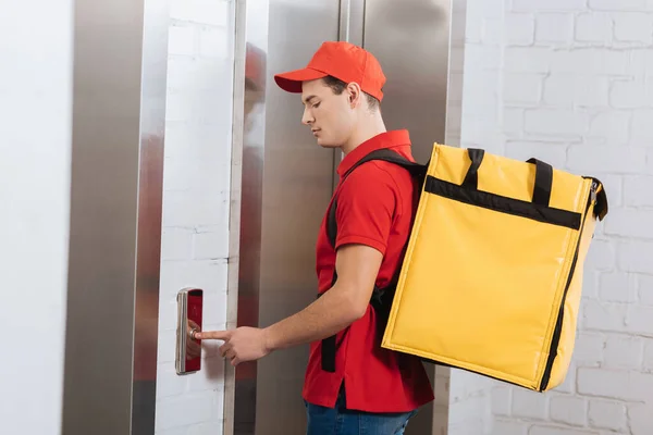 Side view of courier with thermo backpack pressing elevator button — Stock Photo
