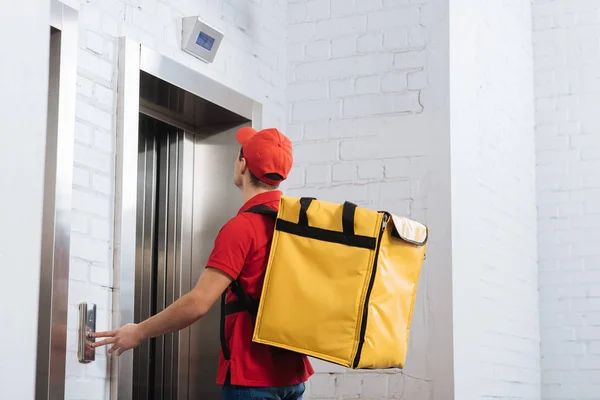 Вид сбоку доставщика с терморюкзаком, нажавшим кнопку лифта — стоковое фото