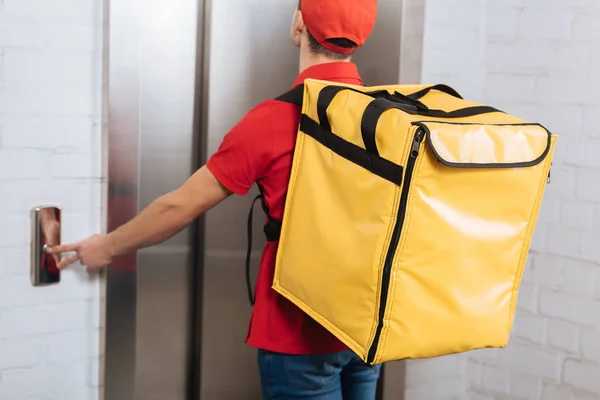 Visão traseira do homem de entrega em uniforme vermelho com mochila térmica pressionando o botão do elevador — Fotografia de Stock